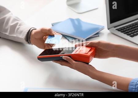 Männliche Hand mit Kreditkarte und Arzt bezahlt über Terminal in der Klinik Stockfoto