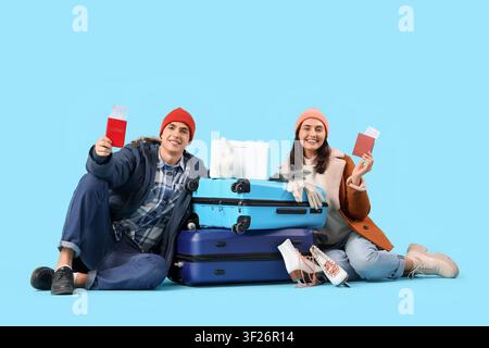 Nettes junges Paar mit Laptop, Koffern, Pässen und Reiseaccessoires auf blauem Hintergrund. Winterurlaubskonzept Stockfoto