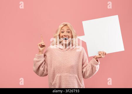 Glückliche junge Frau lächelt und zeigt mit leerem Sprechblasen-Hintergrund im Studio Stockfoto