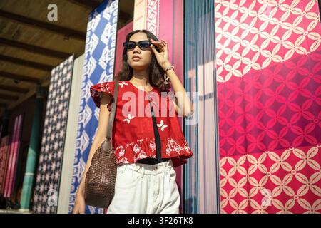 Niedriges Porträt einer stilvollen indonesischen Frau, die moderne Batikbekleidung trägt, vor farbenfrohen Batikausstellungen in Malioboro Yogyakarta. Stockfoto