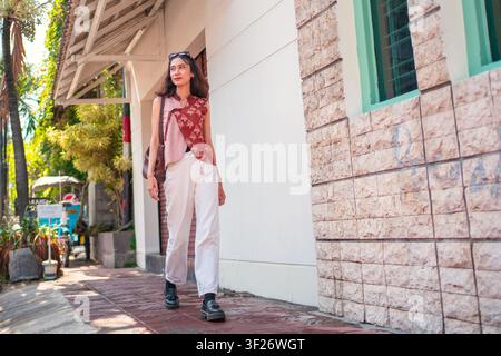 Stylische indonesische Frau, die selbstbewusst im Freien läuft und moderne Batik-Mode trägt. Urbaner Lebensstil und kulturelles Modekonzept. Stockfoto