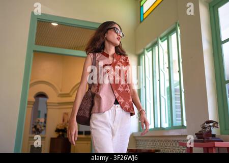 Niedrigwinkelaufnahme einer stilvollen indonesischen Frau, die moderne Batikmode im Innenraum trägt. Selbstvertrauen und zeitgenössisches Lebensstilkonzept. Stockfoto
