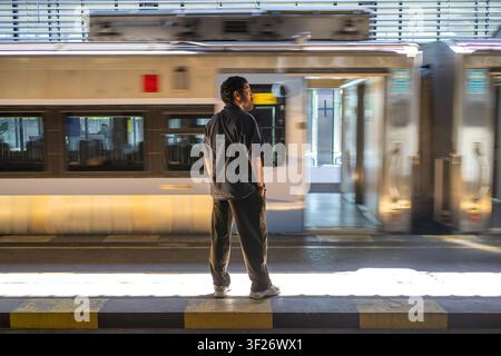 Indonesischer Mann steht auf einem Bahnhofsgleis, während ein Zug vorbeifährt. Öffentlicher Verkehr, Geduld und städtisches Pendeln Konzept. Stockfoto