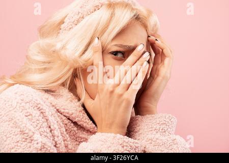 Besorgte junge Frau, die ihr Gesicht mit den Händen bedeckt, rosa Hintergrund, Emotionskonzept Stockfoto