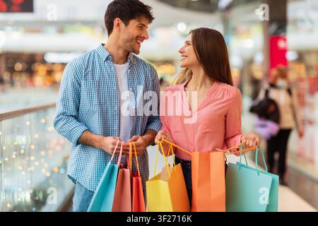 Glückliches junges Paar, das zusammen in der Einkaufsmall mit bunten Einkaufstüten einkauft Stockfoto