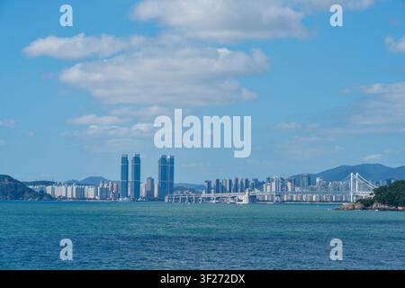 Ein malerischer Weitwinkel-Panoramblick auf die Stadtlandschaft von Busan mit der Gwangan-Brücke, die sich über den blauen Ozean unter einem teilweise bewölkten Himmel erstreckt. Stockfoto