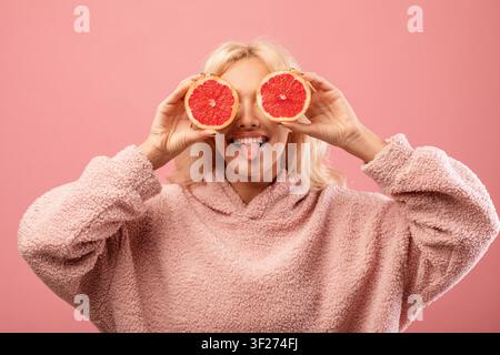 Zufriedenste junge Frau hält Grapefruitscheiben, rosa Hintergrund, Konzept für Gewichtsabnahme Stockfoto