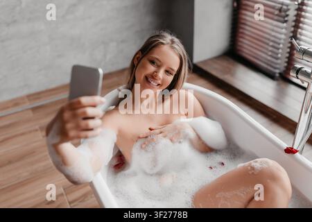 Junge Frau genießt ein entspannendes Schaumbad und macht ein Selfie in einem modernen Badezimmer Stockfoto