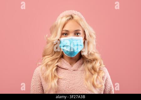Junge Frau mit blauer medizinischer Maske, lächelnd, rosa Hintergrund, Gesundheitskonzept Stockfoto
