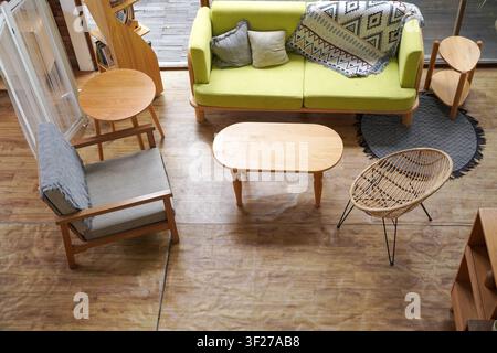 Oberblick auf ein stilvolles Wohnzimmer mit einem grünen Sofa, einem Rattanstuhl und einem Holzkouchentisch in einem hellen, gemütlichen Raum. Stockfoto