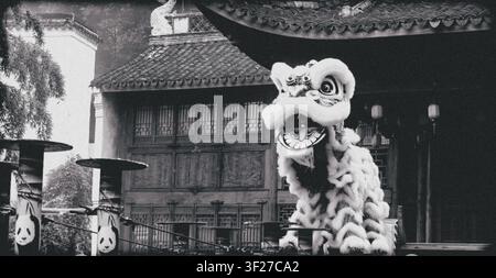 Schwarzweißfoto eines traditionellen chinesischen Drachentanzkostüms vor einem alten Tempelgebäude, das kulturelles Erbe, Feier und Geschichte zeigt Stockfoto