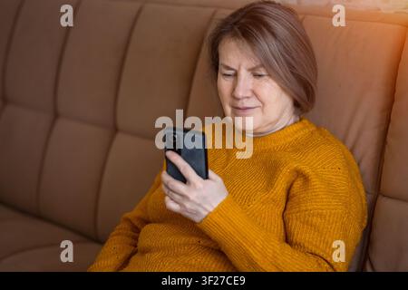 Seniorin, die ein Smartphone benutzt, sitzt auf dem Sofa zu Hause Stockfoto