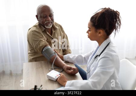 Senior Schwarzer Mann, der in einer Klinik von einer Ärztin den Blutdruck messen lässt, Gesundheitskonzept Stockfoto
