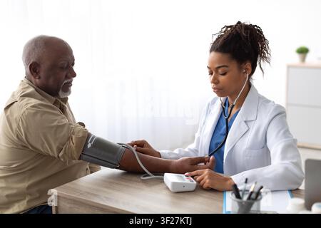 Senior Afroamerikaner, dessen Blutdruck von einer Krankenschwester in der Klinik gemessen wird, Gesundheitskonzept Stockfoto