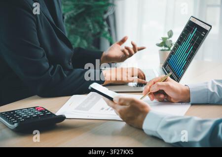 Geschäftsleute diskutieren über ein Finanzdashboard auf dem Laptop mit Taschenrechner, Smartphone und Berichtsunterlagen, was Buchhaltungsanalysen darstellt Stockfoto