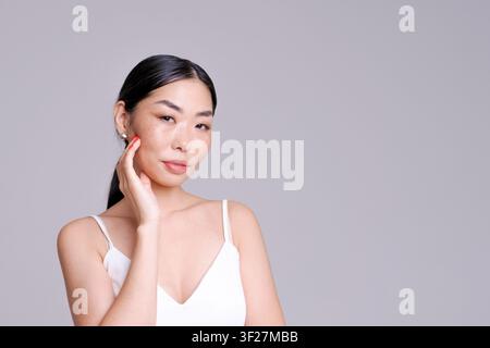 Junge asiatische Frau Schönheitsporträt mit natürlichen Sommersprossen, die in einem hellen Studio weg schaut. Geeignet für Hautpflege, natürlichen Glanz und Kosmetik-Inhalte. Stockfoto