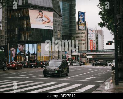 Taxi überquert eine Kreuzung mit großen Werbetafeln im Einkaufsviertel Ginza, Chuo, Tokio, Japan Stockfoto