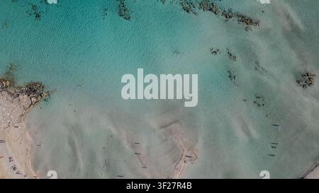 Horizontale Luftansicht von oben auf den Strand von Elafonisi auf Kreta, Griechenland, mit kristallklarem türkisblauem Meer und Touristen, die sich in der Nähe von Sonnenschirmen entspannen Stockfoto