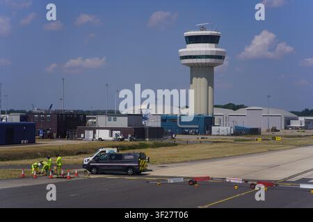 Flughafen Gatwick Luftfahrtkontrollturm mit Bodenpersonal in Hochsicherheitswesten, das in der Nähe von Fahrzeugen und einem TUI Airways-Flugzeug im Hintergrund arbeitet Stockfoto