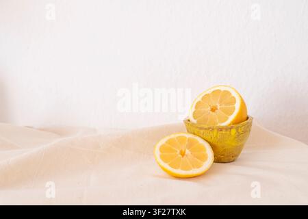 Komposition mit Zitronen in einer gelben handgefertigten Keramiktasse auf einem beigefarbenen Textilhintergrund. Stockfoto