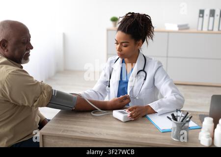 Schwarzer männlicher Patient, dessen Blutdruck von einer Ärztin in einer Gesundheitsambulanz überprüft wird Stockfoto