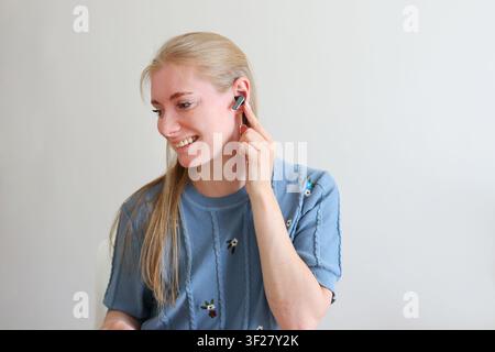 Frau, die einen True-Wireless-Kopfhörer einsetzt, während sie die Ladestation hält, moderne Audiotechnologie und täglicher Lebensstil. Stockfoto