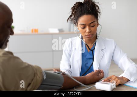 Afroamerikanische Krankenschwester misst den Blutdruck eines männlichen Patienten in der Klinik, Gesundheitskonzept Stockfoto