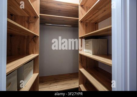 gut organisierter begehbarer Kleiderschrank mit Holzregalen. Auf den Regalen stehen ordentlich Aufbewahrungsboxen. Die Innenwände sind in einer neutralen Farbe gestrichen Stockfoto
