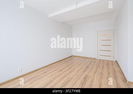 heller, leerer Raum mit weißen Wänden, einem hellen Holzboden und einer Tür mit horizontalen Paneelen Stockfoto