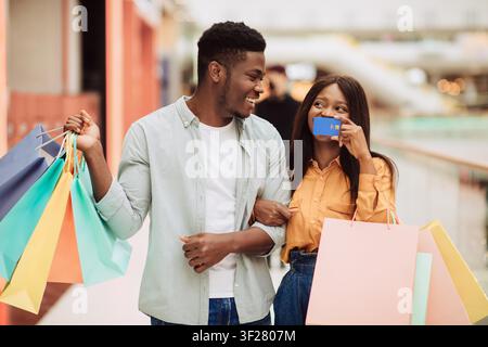 Glückliches schwarzes Paar, das zusammen mit bunten Taschen in der Einkaufs mall einkauft und Qualitätszeit verbringt Stockfoto