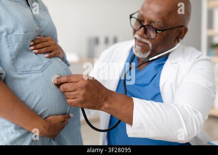Arzt untersucht den Bauch einer schwangeren schwarzen Frau mit einem Stethoskop in einer Gesundheitsklinik Stockfoto