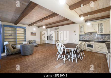 Heller Wohn-/Essbereich mit Holzböden, Balkendecke, Sofas und einer Küche mit Schränken und einem Esstisch Stockfoto