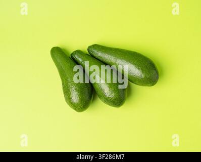 Avocado isoliert, ganzer Avokado-Satz, drei grüne Avocados gestapelt, frische Alligatorbirne, Guacamole-Zutaten, lange Avocado-Frucht auf grünem Hintergrund Stockfoto