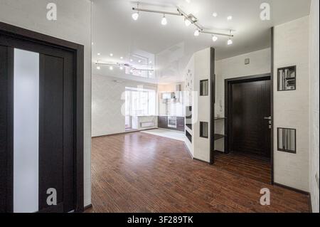 Modernes Apartment-Interieur mit dunklen Holzböden, schlanken weißen Wänden und stilvoller Beleuchtung. Offenes Konzept führt zu einem Küchenbereich Stockfoto