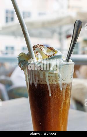 Irische Kaffee mit Schlagsahne in einem hohen Glas auf dem Cafétisch am Fenster Stockfoto