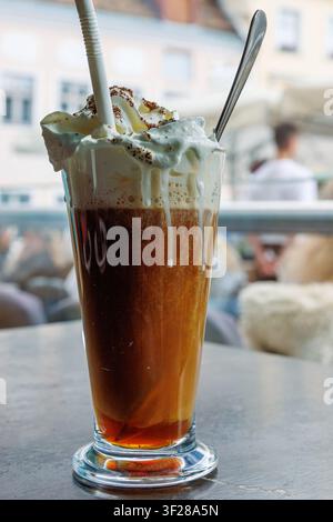 Irische Kaffee mit Schlagsahne in einem hohen Glas auf dem Cafétisch am Fenster Stockfoto