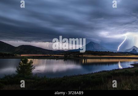 Blitze zucken über einen See und Berge in der Nacht Stockfoto