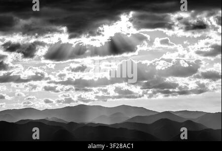 Sonnenstrahlen brechen durch dramatische Wolken über Bergen Stockfoto