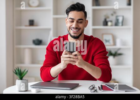 Lächelnder junger Mann, der im modernen Büro ein Smartphone verwendet, Geschäftskonzept Stockfoto