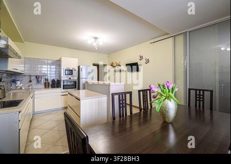 heller Küchen-Essbereich mit einem dunklen Holztisch, Tulpen und modernen Geräten. Der Stil ist sauber und gemütlich Stockfoto