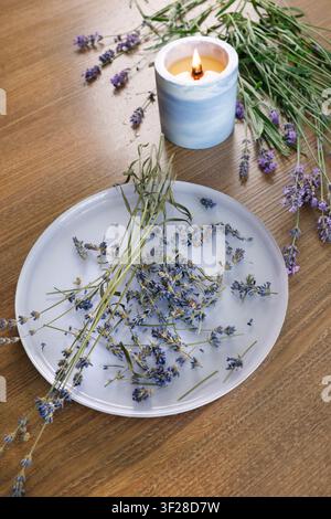 Brennende Kerze blaues Keramikgefäß getrocknete Lavendelblütenplatte Holztablett. Top-Down-Ansicht vertikaler Rahmen Kopierraum Hintergrundvorlage. Aromatherapie Zuhause Stockfoto
