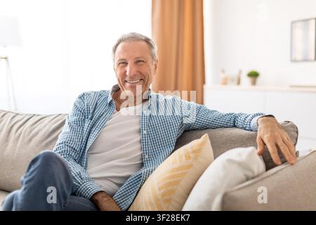 Zufriedener älterer kaukasischer Mann lächelt zu Hause, entspannt auf dem Sofa, Lebensstilkonzept Stockfoto
