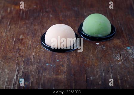 Zwei rosa und grüne traditionelle japanische Mochi oder asiatische Wagashi, Reiskuchen. Leckere Süßigkeiten, Dessert auf braunem Holzuntergrund Stockfoto