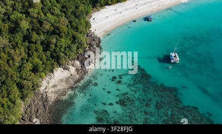 Luftaufnahme von Whitehaven Beach mit türkisblauem Wasser, Korallenriffen, einer in der Bucht vor Anker liegenden Katamarang und üppigem tropischen Wald entlang der felsigen Küste Stockfoto