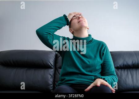 Frau sitzt auf einem Sofa, leidet unter Kopfschmerzen und fühlt sich unwohl Stockfoto