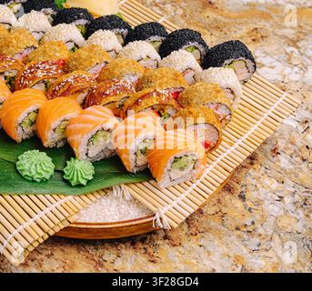 Eine bunte Auswahl an Sushi-Rollen, ordentlich auf einer Bambusmatte angeordnet. Das Tablett enthält verschiedene Arten von Rollen mit frischem Fisch, Gemüse und Garnierungen. Stockfoto