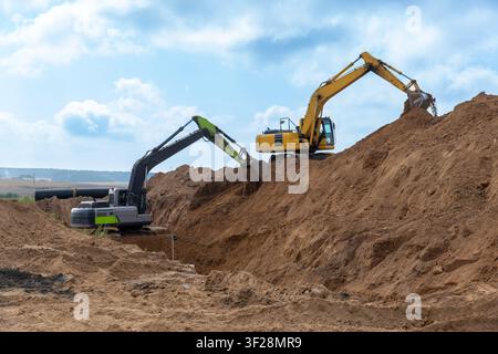 Zwei Bagger, die auf einer Baustelle arbeiten, Erde bewegen und tiefe Gräben ausheben. Industrieprojekt mit schwerer Baumaschinerie an einem sonnigen Tag. Stockfoto