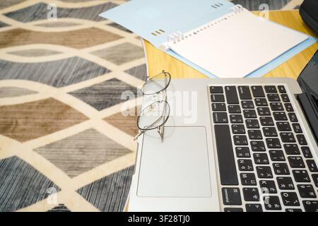 Nahaufnahme von runden Brillen, die auf einem Laptop ruhen, mit einem Notizbuch daneben, perfekt für Studium, Homeoffice und Produktivitätskonzepte. Stockfoto
