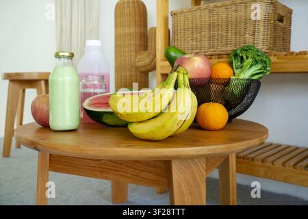 Frische Bananen mit verschiedenen Früchten und gesunden Smoothie-Flaschen, die auf einem Holztisch arrangiert sind, ideal für gesunde Ernährung und Ernährungs konzepte. Stockfoto