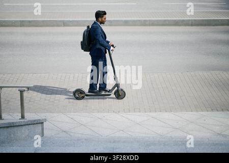 Indischer erwachsener Geschäftsmann, der mit dem Elektoroller zur Arbeit pendelt Stockfoto